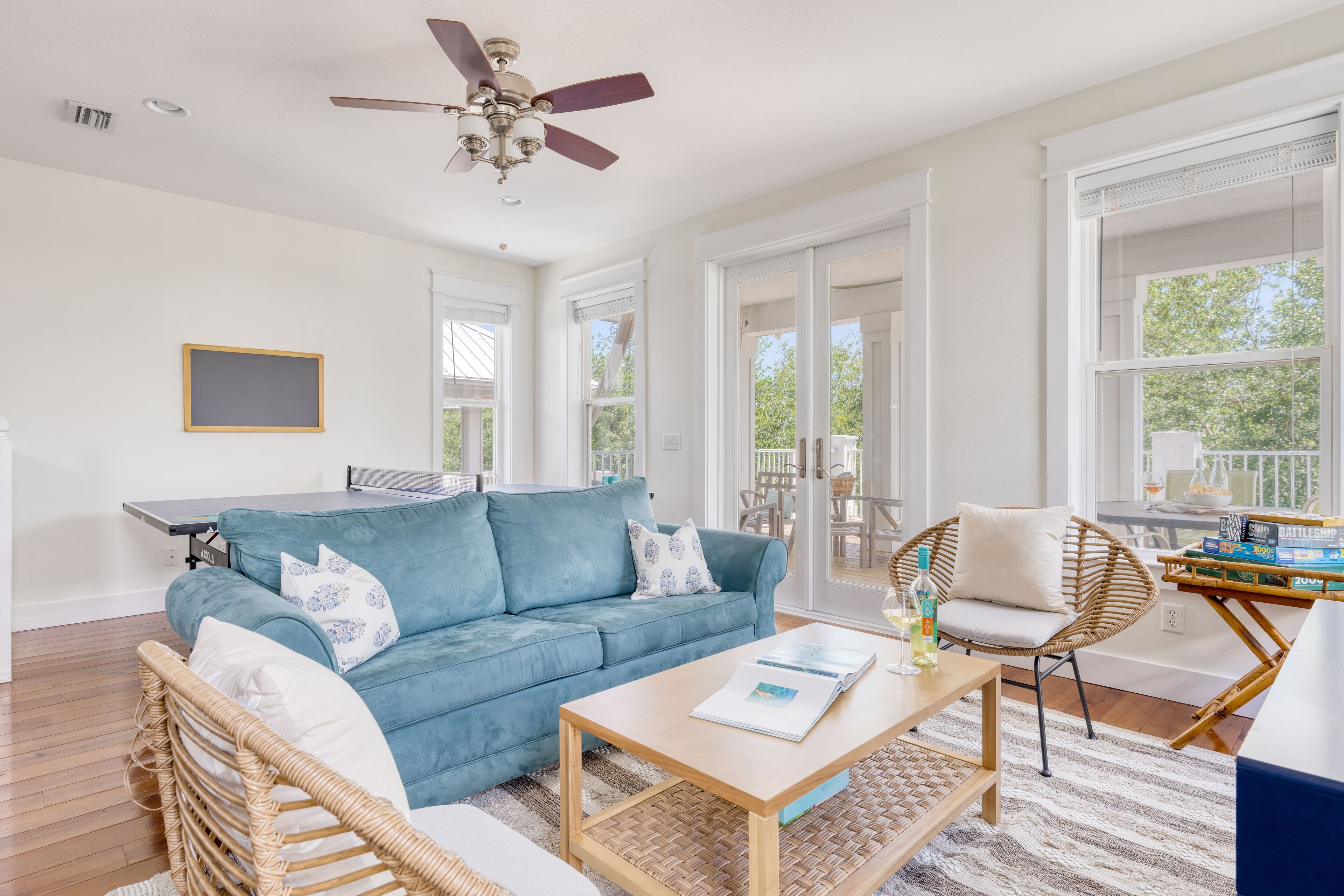 A spacious living room with a blue sofa, a wooden coffee table, wicker chairs, and a ceiling fan.