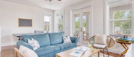 A spacious living room with a blue sofa, a wooden coffee table, wicker chairs, and a ceiling fan.