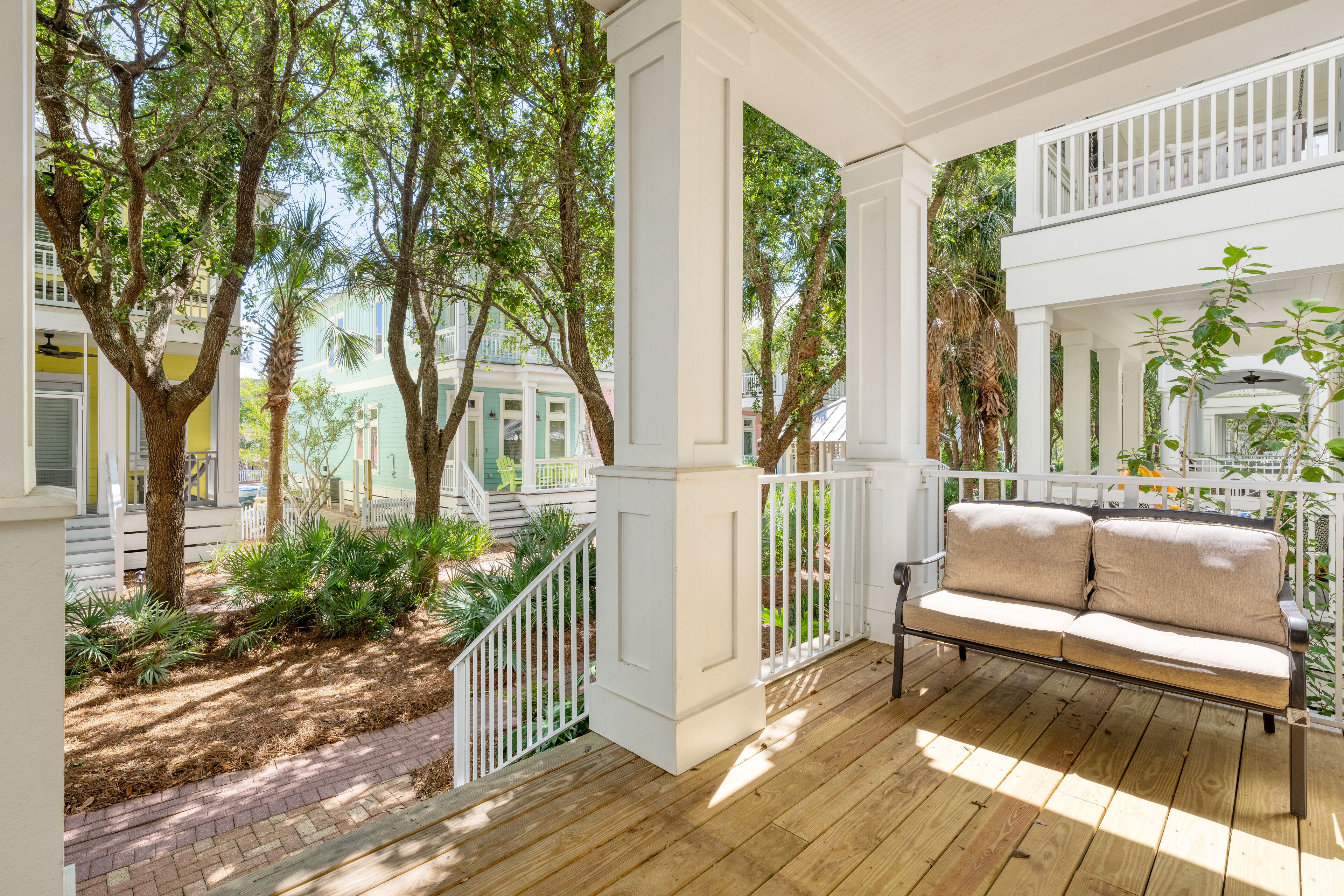 Una terraza de madera con barandilla blanca, un sofá color crema y vistas de edificios y árboles circundantes.