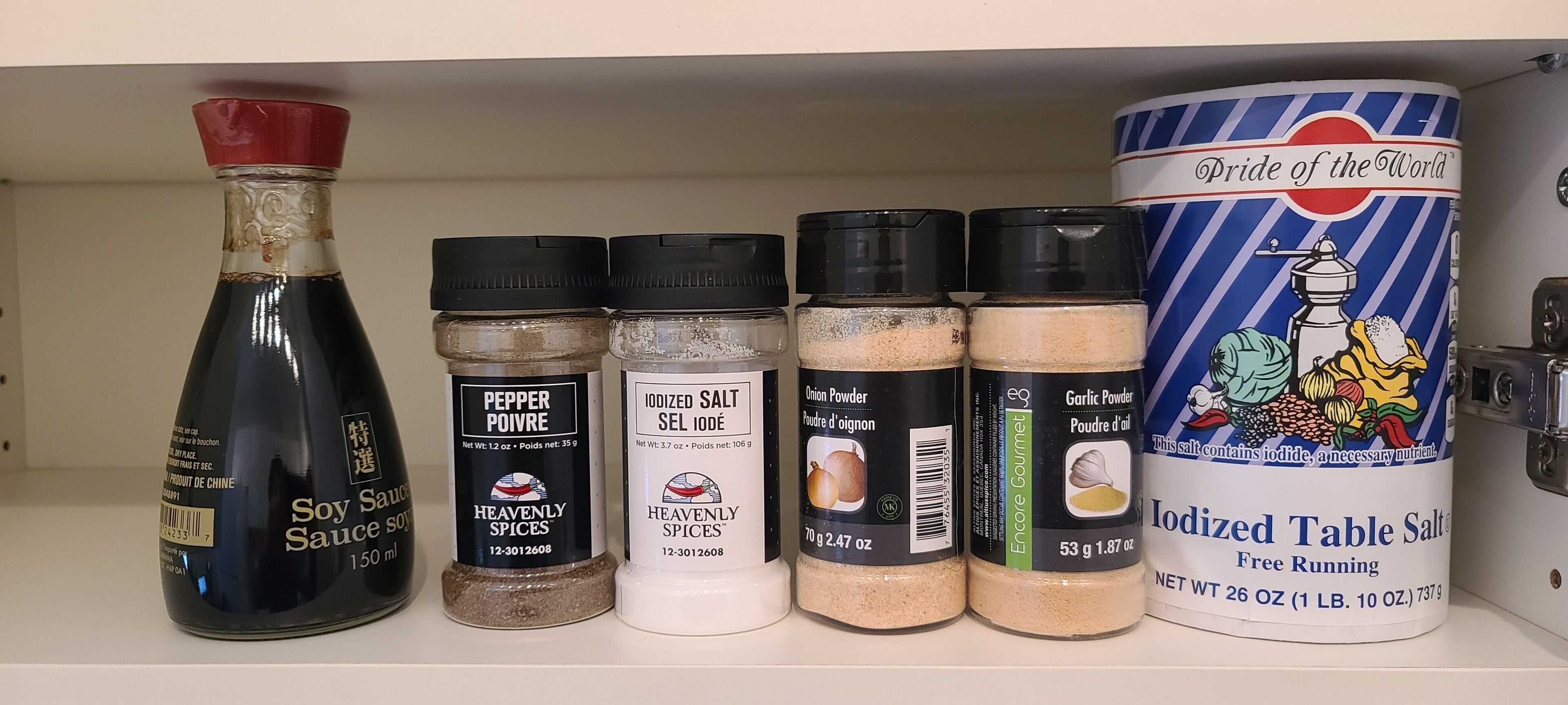 Une étagère contenant divers récipients d’épices, notamment de la sauce soja, du poivre en poudre, du sel iodé, de l’oignon en poudre, de l’ail en poudre et du sel de table iodé.