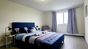 Een slaapkamer met een bed, nachtkastje, lamp en een raam met gordijnen.