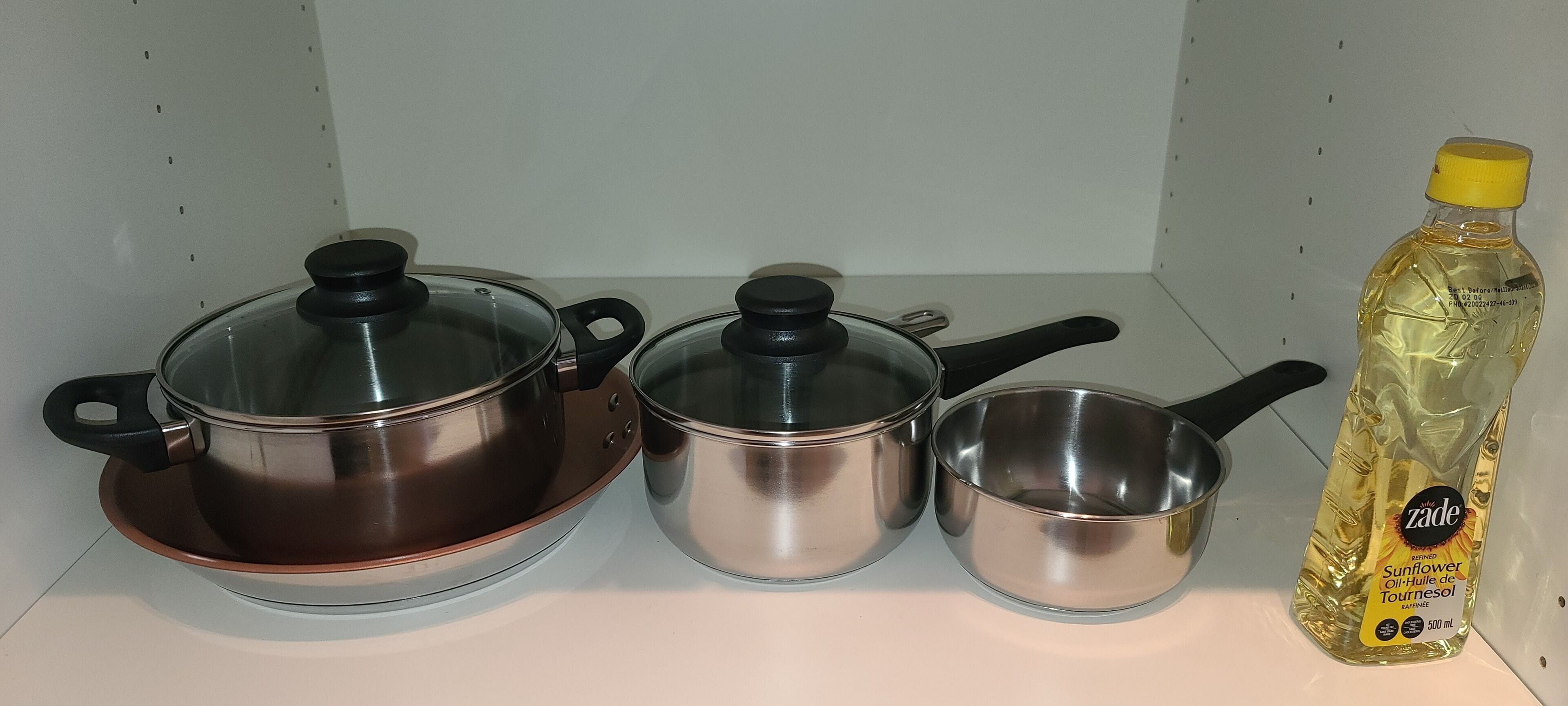 Three stainless steel pots with lids on a white shelf.