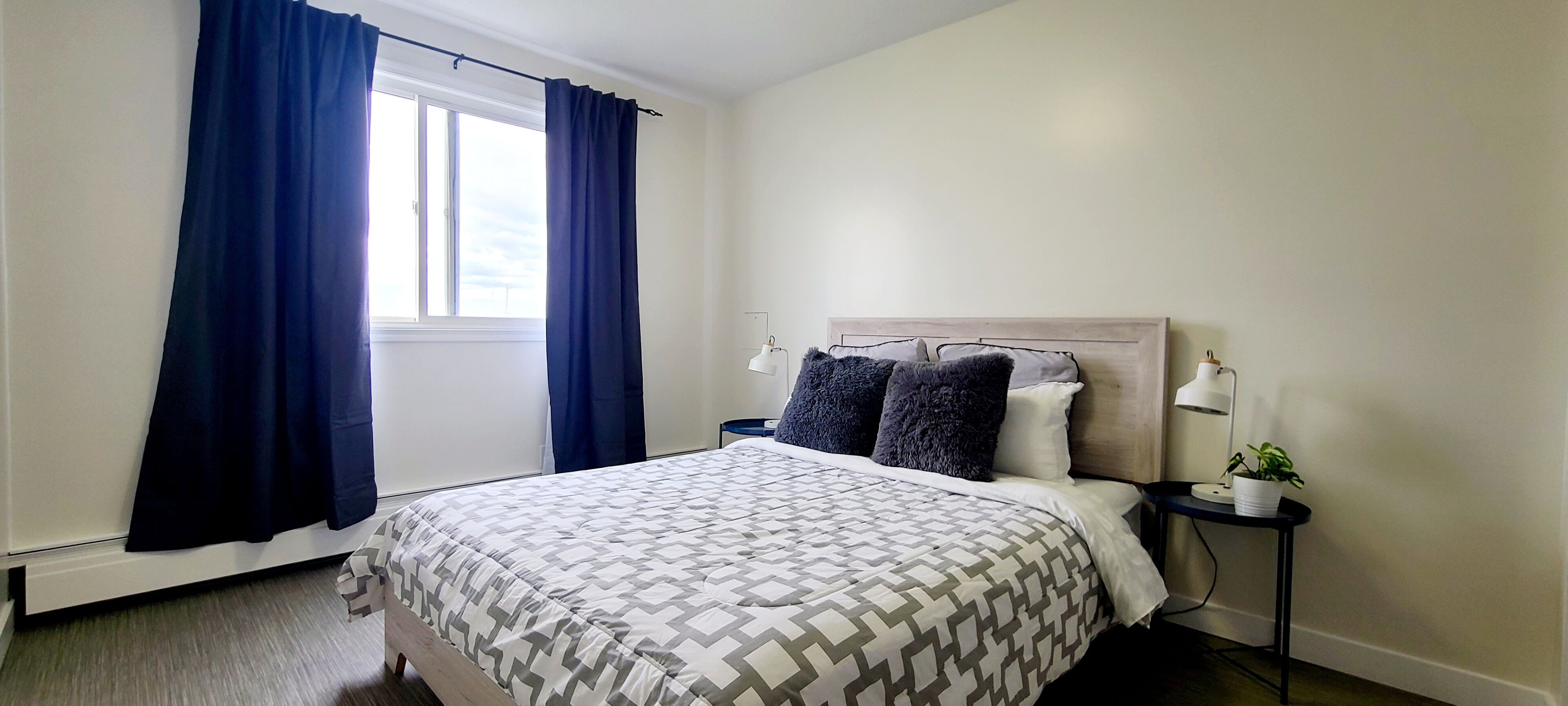 A bedroom with a bed, a nightstand, a lamp, and a window with curtains.