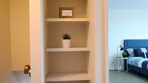 Een modern appartement met een inbouwkast met meerdere planken, een welkomstbord en een kleine potplant.