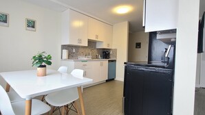 Een kleine keuken met witte kastjes, een zwarte koelkast en een eettafel met witte stoelen.