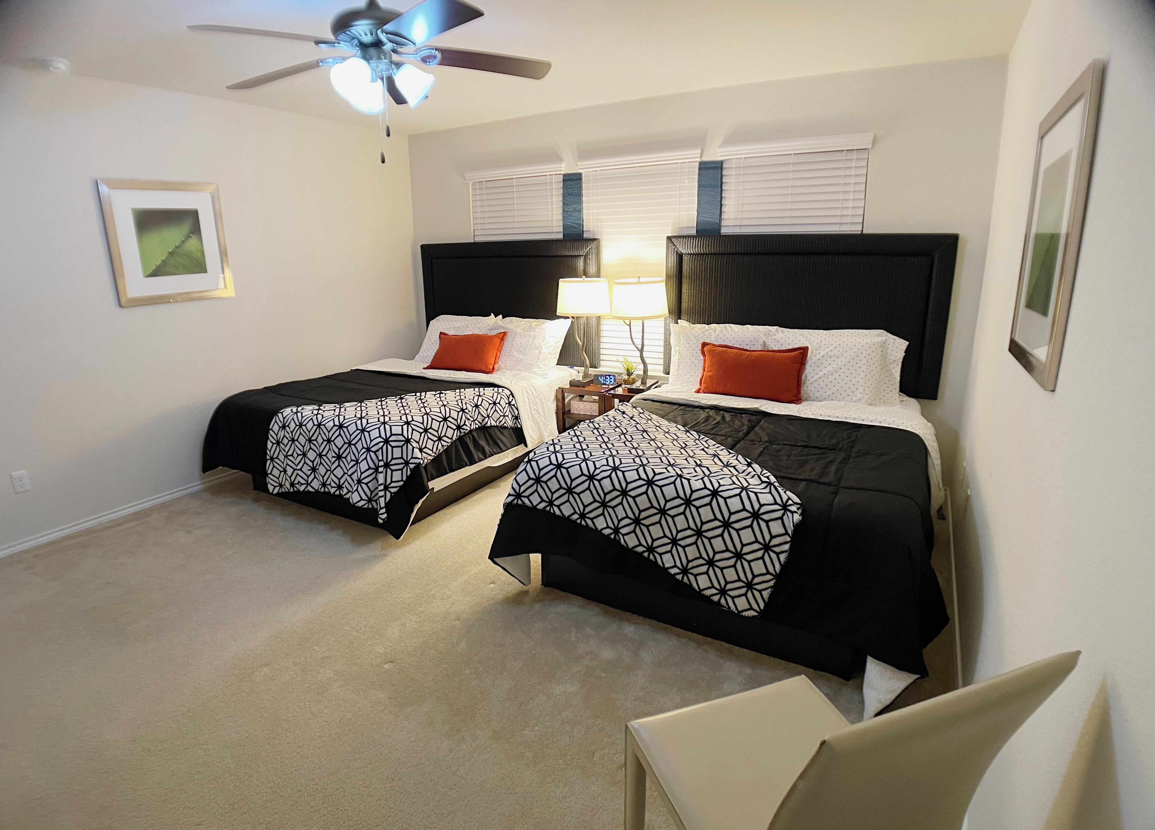 A hotel room with two beds, a ceiling fan, a nightstand with a lamp, and a framed picture on the wall.