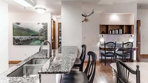 A kitchen with granite countertops, a sink, and a dining area with chairs and a table. - Cozy Suite, Sleeps 6・Jacuzzi, View + Resort Perks (Pigeon Forge)