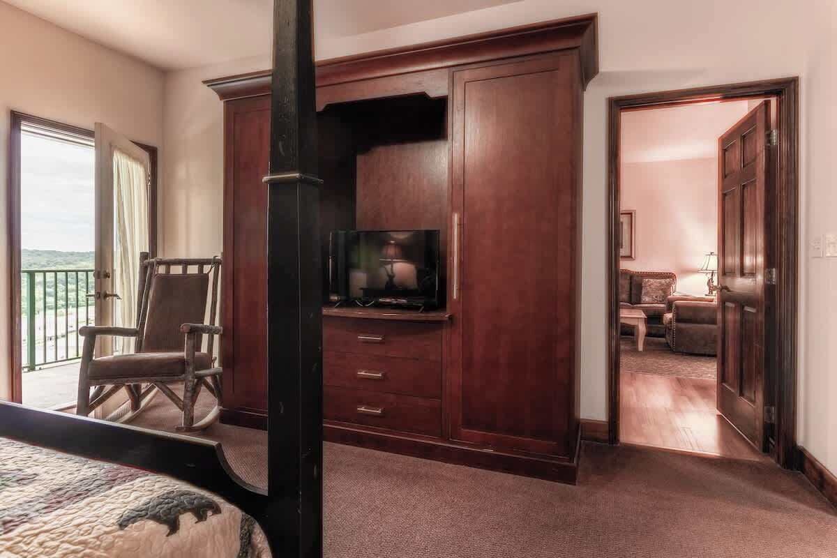 Une chambre à coucher comprenant un lit, un téléviseur, un fauteuil à bascule et une grande armoire en bois.