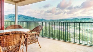 A balcony with wicker chairs and a table, overlooking a green landscape with hills. - Cozy Suite, Sleeps 6・Jacuzzi, View + Resort Perks (Pigeon Forge)