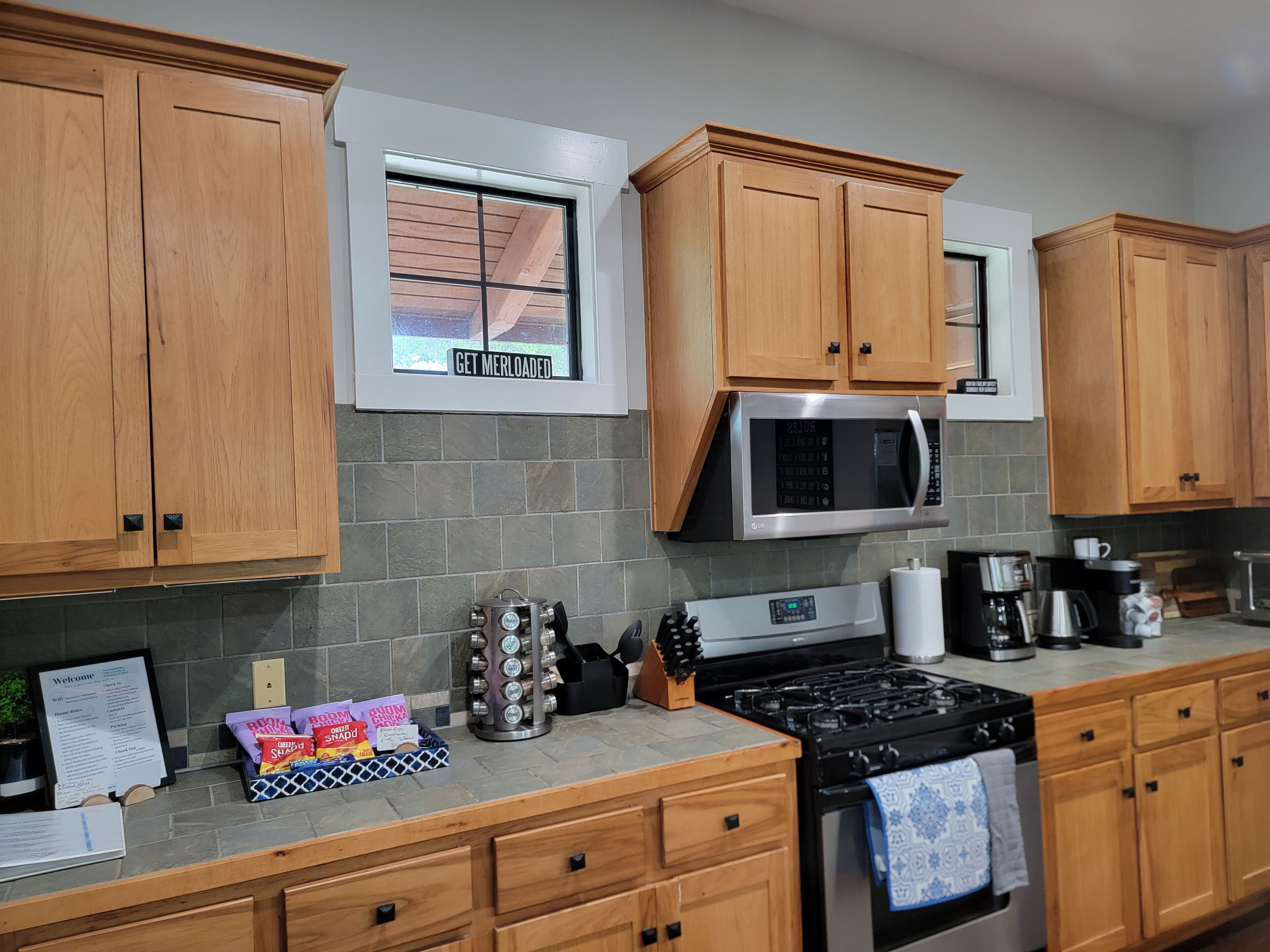 A kitchen with wooden cabinets, a stainless steel microwave, a gas stove, and a window with a sign.