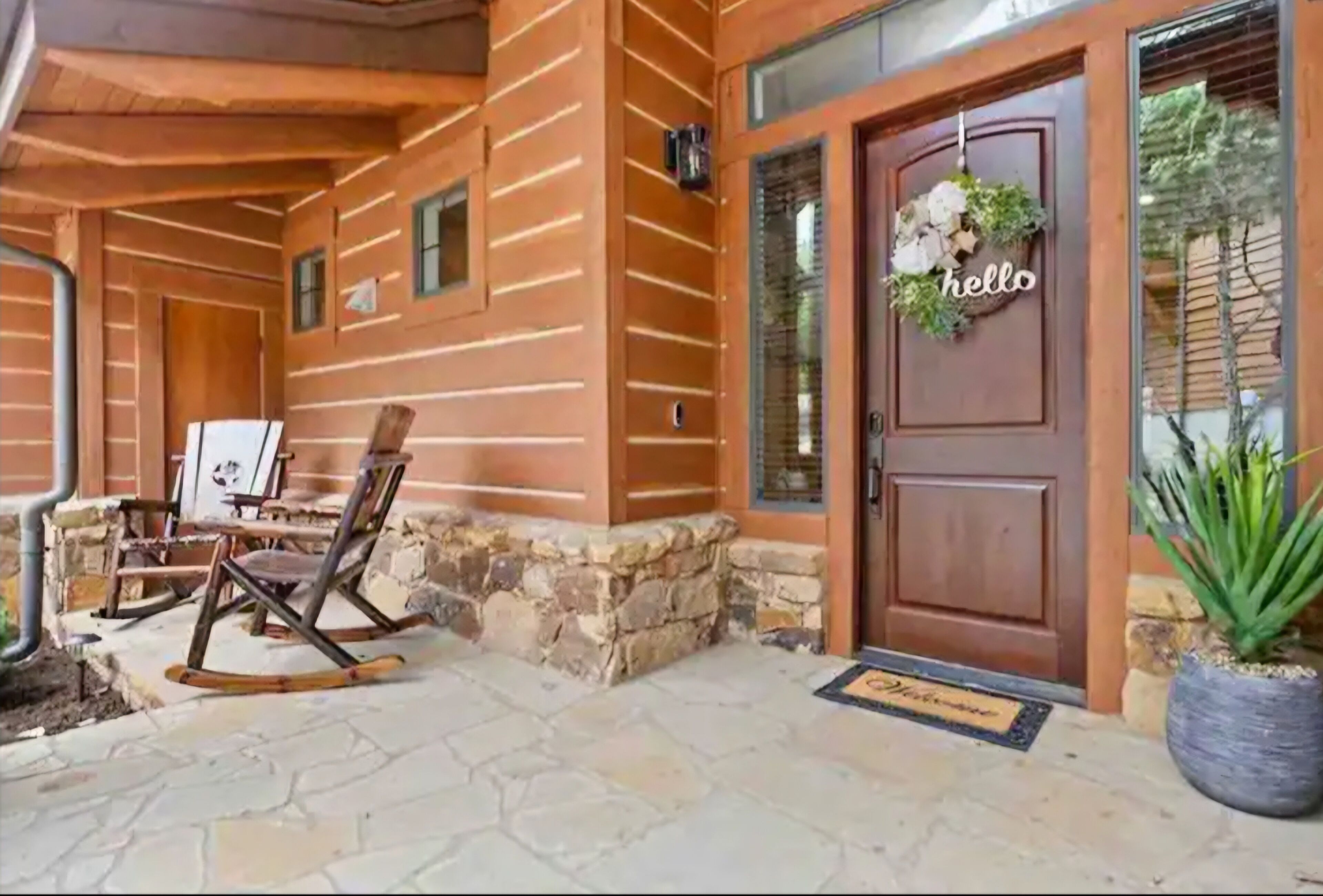A wooden exterior with a stone foundation, a wooden rocking chair, and a door with a 'hello' sign.