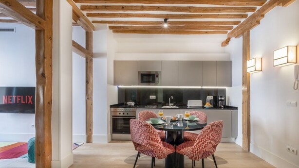 A modern kitchen with a dining area, wooden beams, and a flat-screen TV displaying 'NETFLIX'.