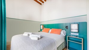 A neatly made bed with pillows and a blanket, a bedside table with a lamp, and a wall-mounted TV.