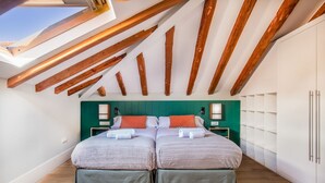 Un dormitorio con dos camas, vigas de madera, tragaluces, pared verde, armarios blancos y suelo de madera.