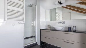 Un baño moderno con cabina de ducha de vidrio, un espejo grande y un mueble de tocador con cajones.