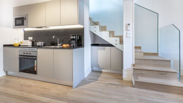 Una cocina moderna con electrodomésticos integrados, una escalera de madera y un diseño minimalista.