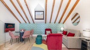 Una sala moderna con techo estilo loft, un rincón de descanso acogedor con un sofá rojo y un sofá gris, una mesa de comedor con sillas estampadas y un televisor montado en la pared.