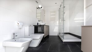 Un baño moderno con un bidé, un inodoro, un lavabo y una ducha con cerramiento de vidrio.