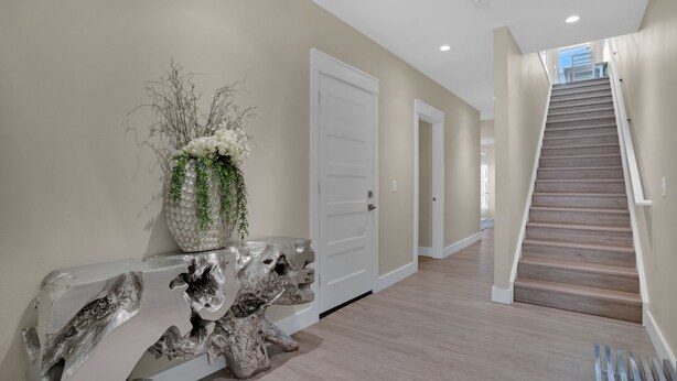 Un pasillo con una escalera de madera, una puerta blanca y una planta decorativa sobre una consola.