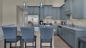 Una cocina moderna con gabinetes grises, electrodomésticos de acero inoxidable y una isla central con taburetes de bar.