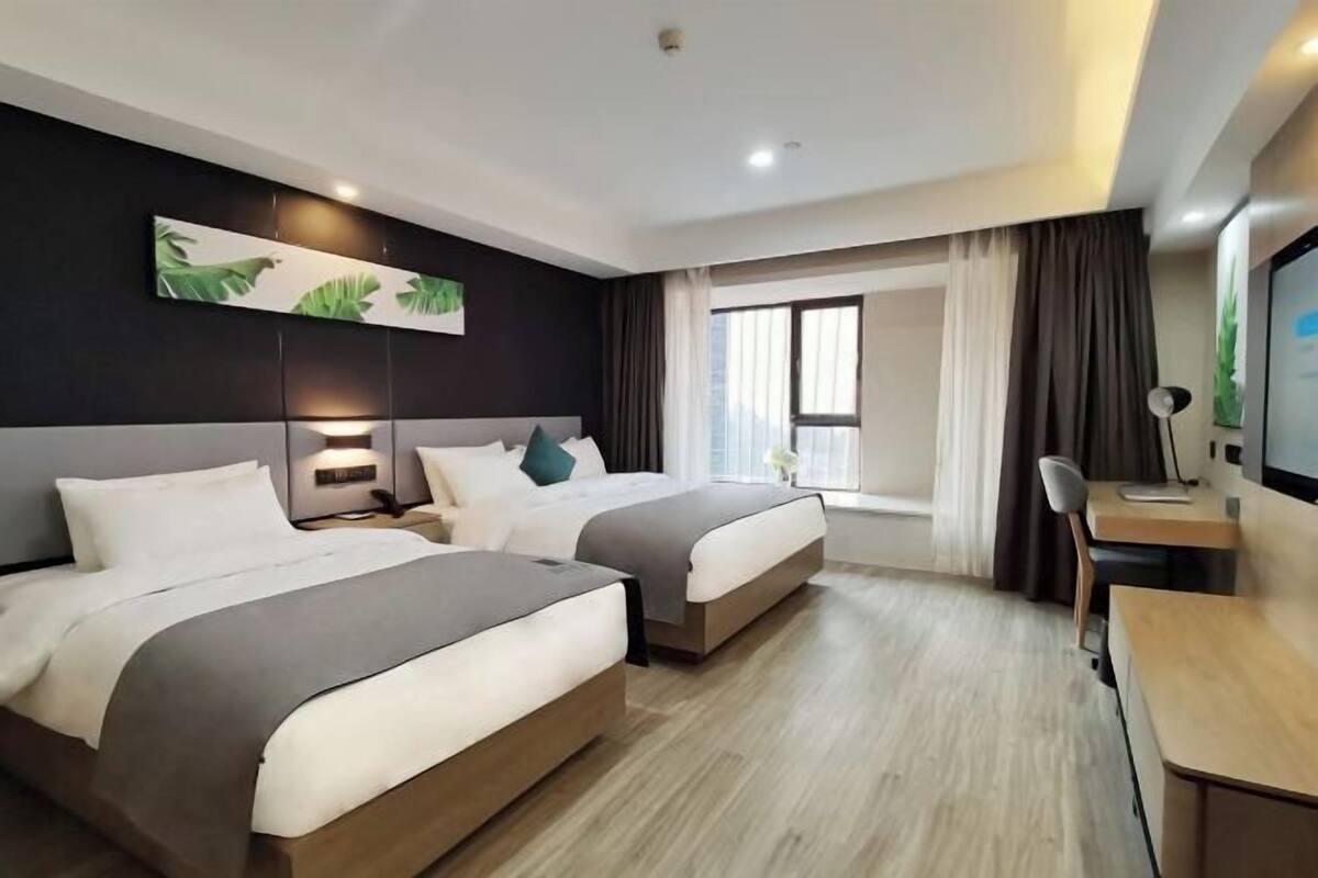Une chambre d’hôtel avec deux lits, un bureau, une chaise, une télévision et une fenêtre avec des rideaux.