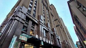 A tall building with a modern architectural design, featuring a prominent entrance with a glass facade and signage indicating a hotel or commercial establishment. - Shankee Tea Style Hotel (Kunming South High-Speed Railway Station Chunrong Street Subway Station) (Kunming)