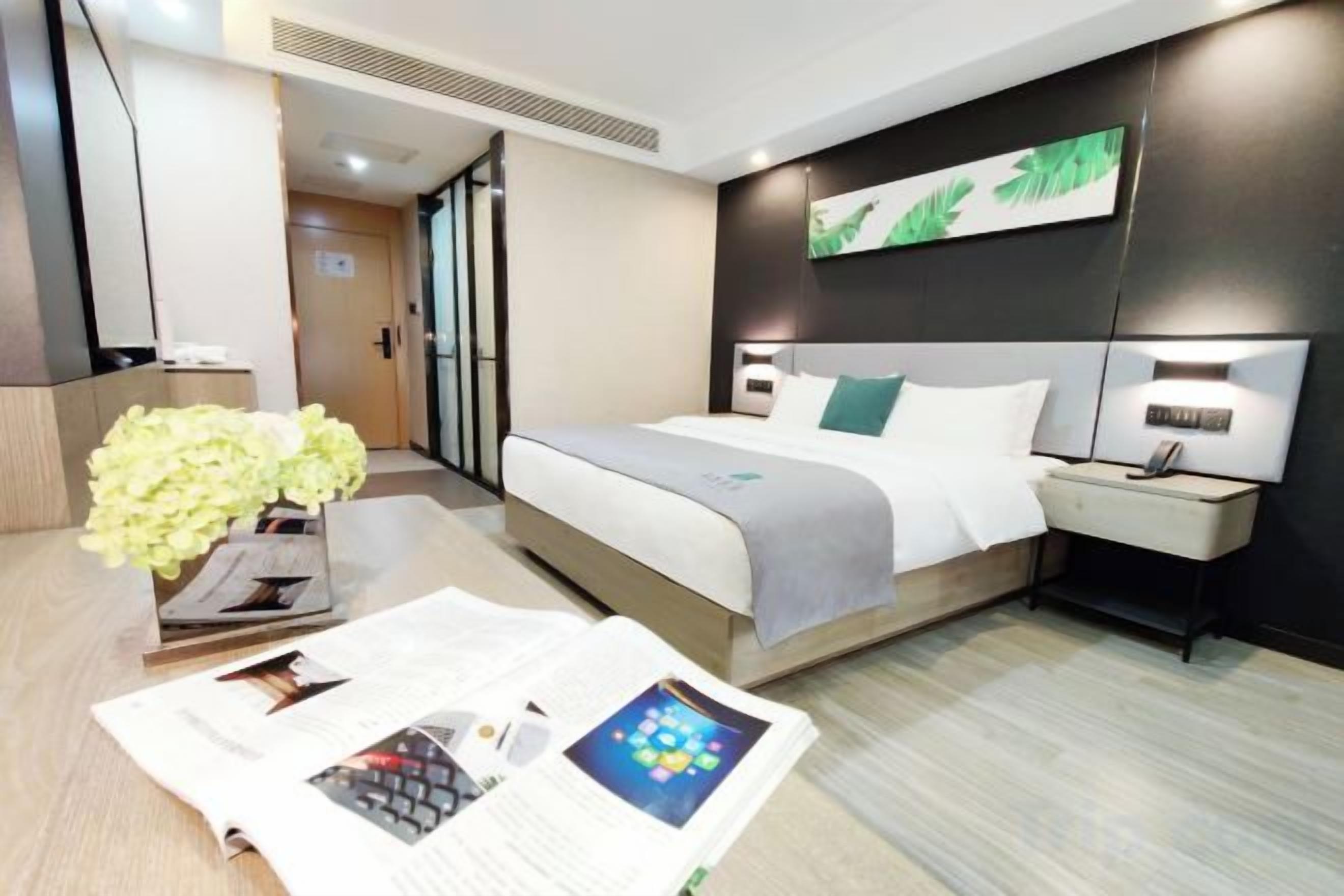 A hotel room with a bed, bedside table, lamp, and a vase with flowers.