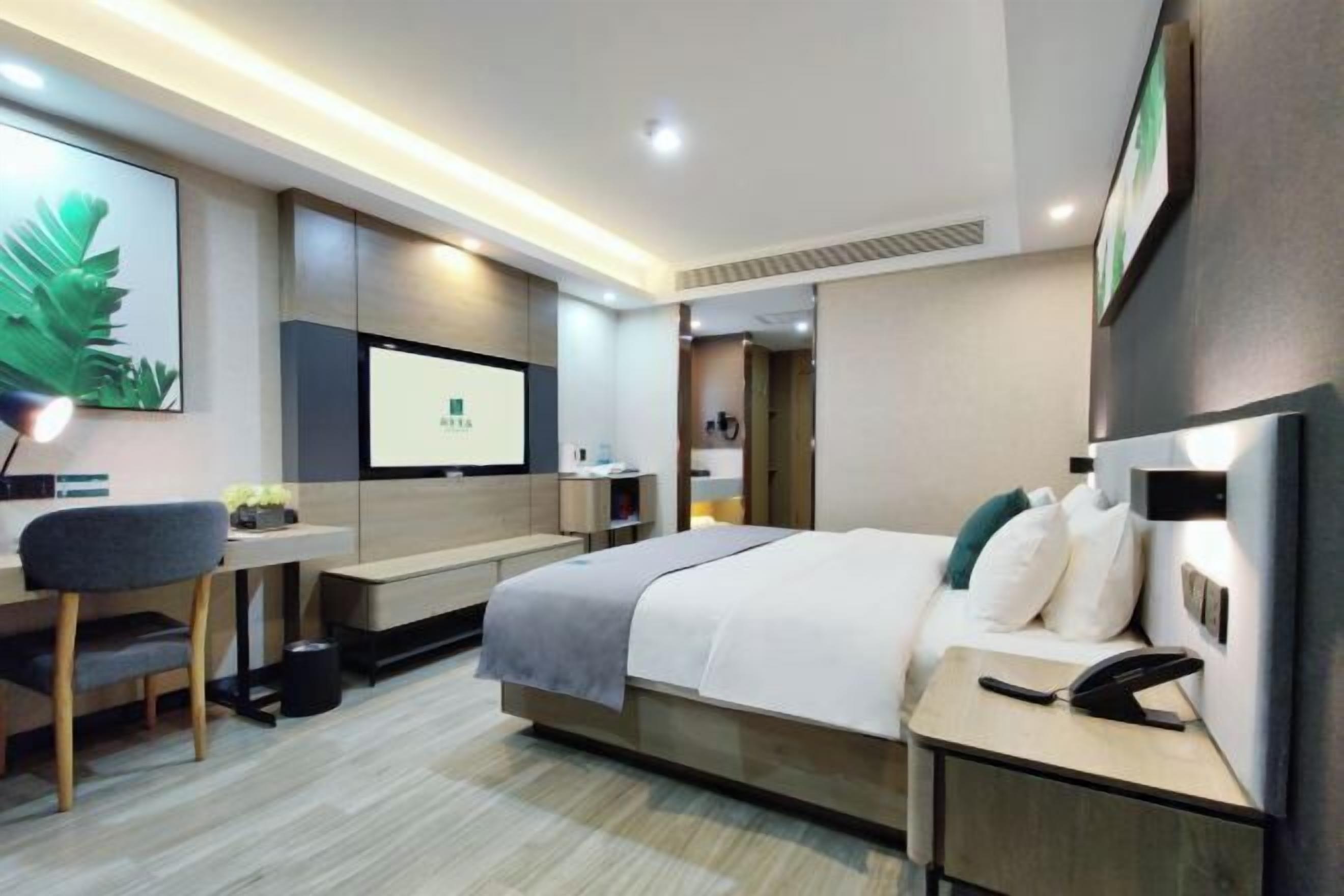 A modern hotel room with a bed, bedside table, desk, chair, and a TV screen.