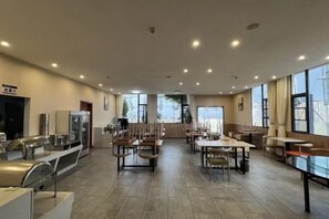 A spacious dining area with multiple tables and chairs, a counter with kitchen appliances, and large windows providing natural light. - Shankee Tea Style Hotel (Kunming South High-Speed Railway Station Chunrong Street Subway Station) (Kunming)