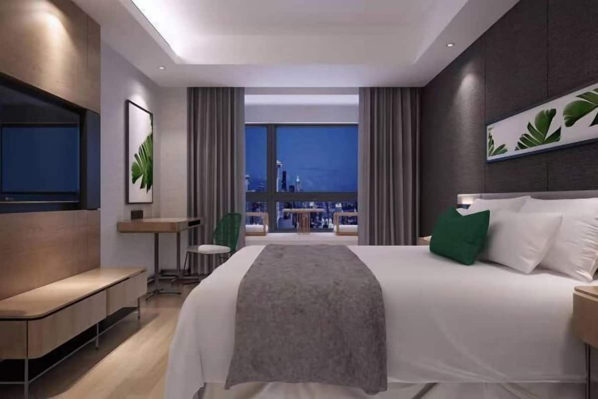 Une chambre d’hôtel moderne dotée d’un grand lit, d’un coin salon, d’une petite table et offrant une vue sur le paysage urbain.