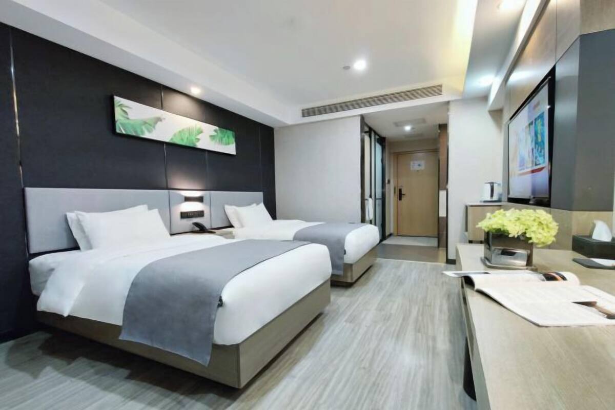 Une chambre d’hôtel moderne avec deux lits, un bureau et un grand miroir.