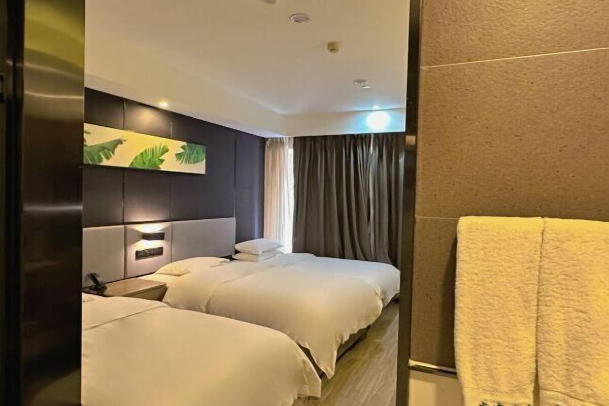 Hotellihuone, jossa on kaksi sänkyä, sängynpääty, jossa on valaisin, seinälle ripustettu taideteos ja pyyhe lattialla.