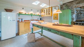 A kitchen with a wooden island, a white refrigerator, and a stone wall. - Secret Cottage, St Ives – Sleeps 6 – Sea Views – Garden (St Ives)