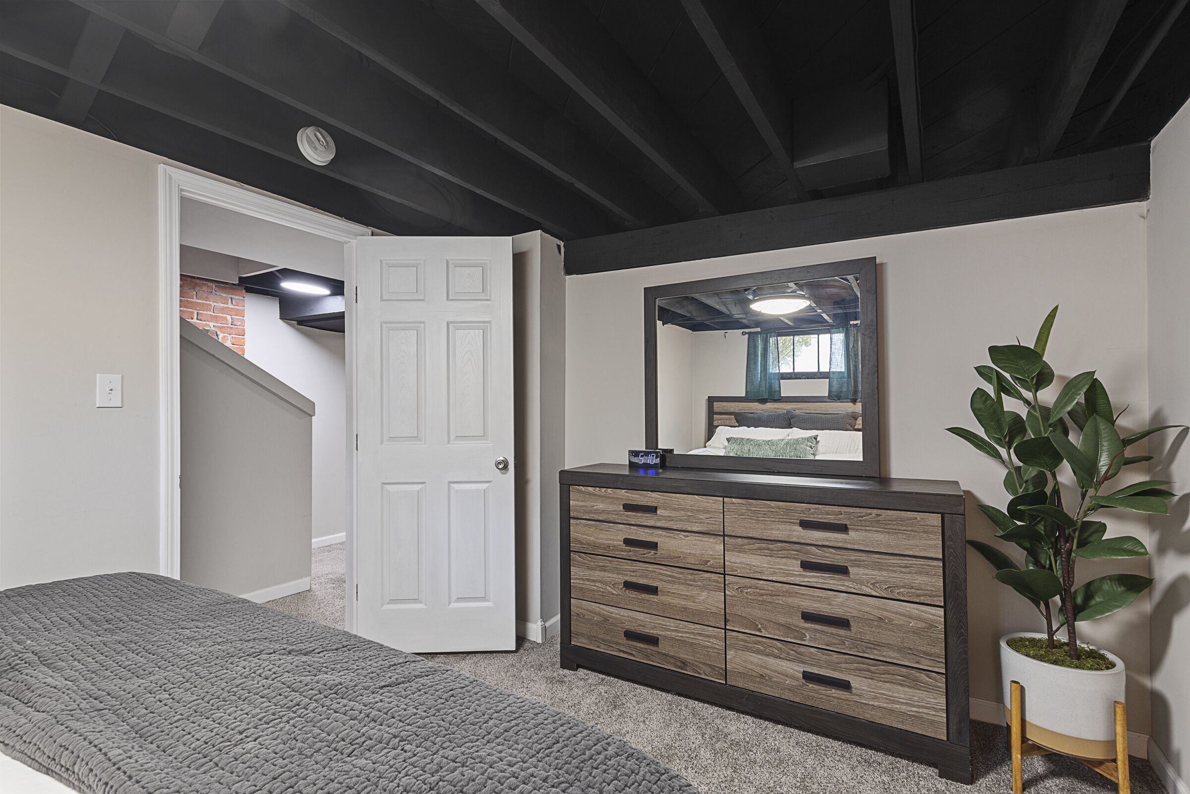 A bedroom with a bed, a dresser, a mirror, and a potted plant.