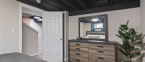 A bedroom with a bed, a dresser, a mirror, and a potted plant.