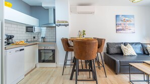 A modern kitchen with a dishwasher, microwave, and stove. There is a dining area with a table and chairs, and a sofa with cushions. - Apartment in the center completely renovated (Empuriabrava)