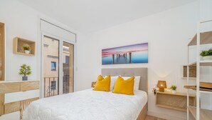 A bedroom with a bed, a nightstand, a shelf with plants, a painting, and a view of the outside. - Apartment in the center completely renovated (Empuriabrava)