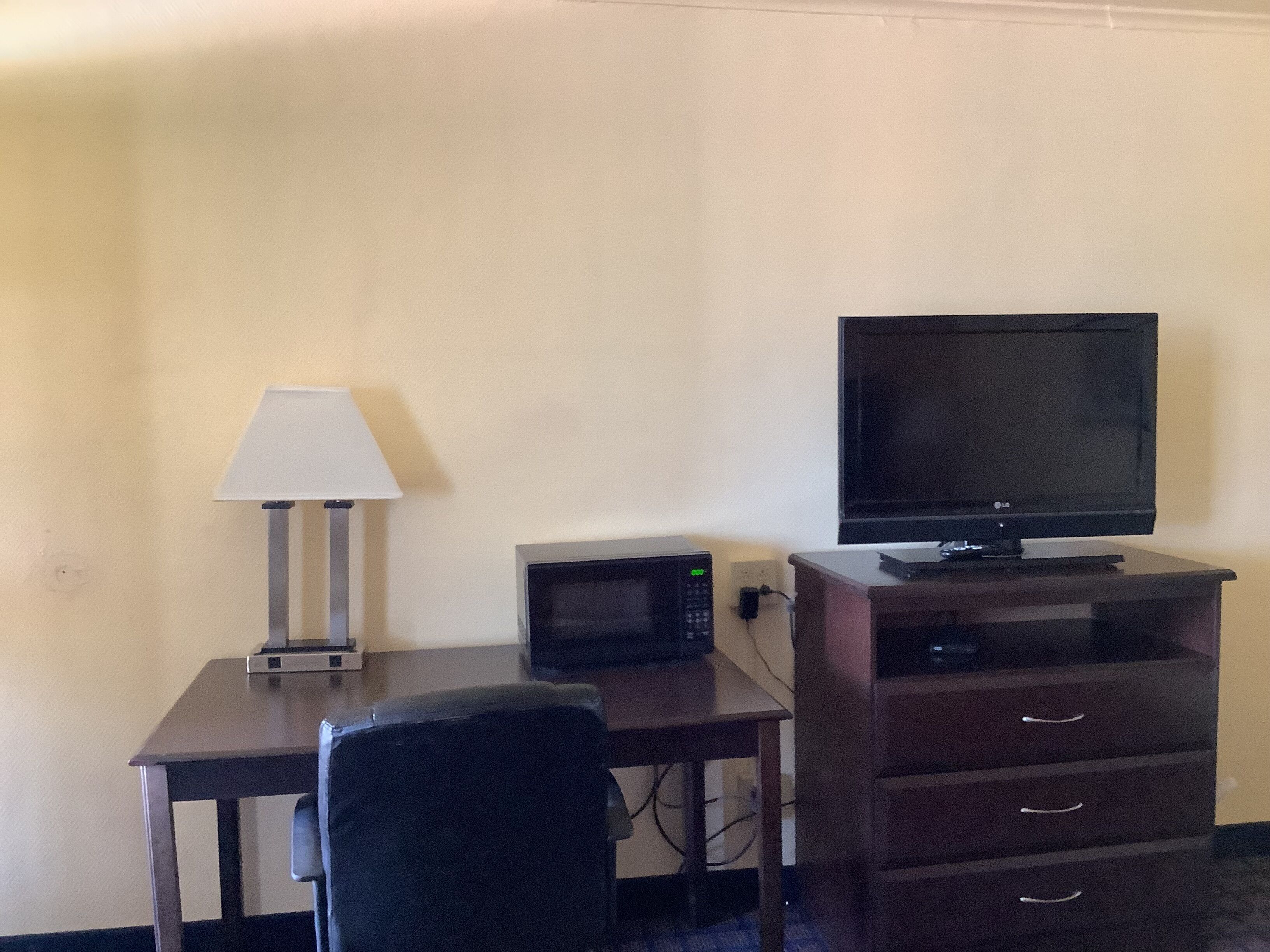 Une chambre d’hôtel équipée d’un bureau, d’une télévision, d’un four à micro-ondes, d’une lampe et d’une chaise.