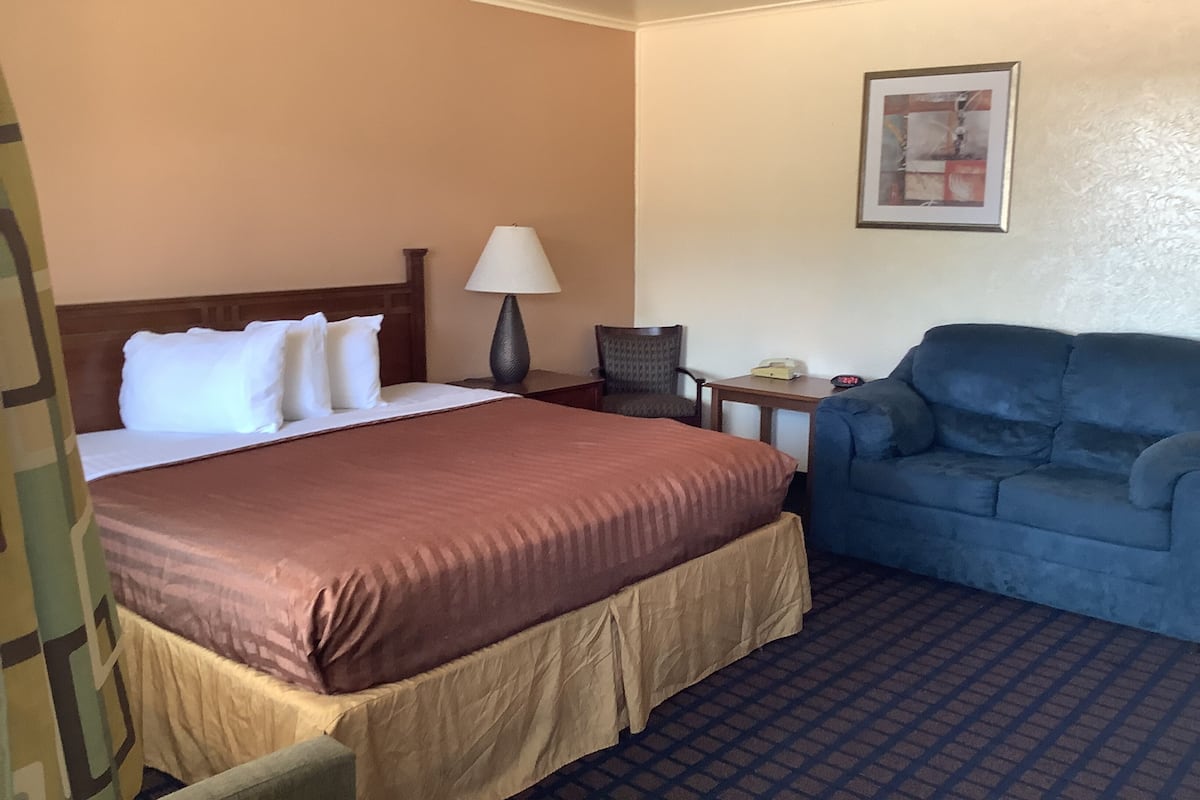 A hotel room with a bed, a desk, a chair, a sofa, and a wall-mounted telephone.