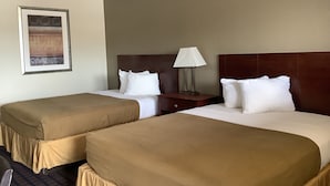 Hotellihuone, jossa on kaksi sänkyä, yöpöytä lampun kanssa ja seinällä oleva kehystetty kuva.