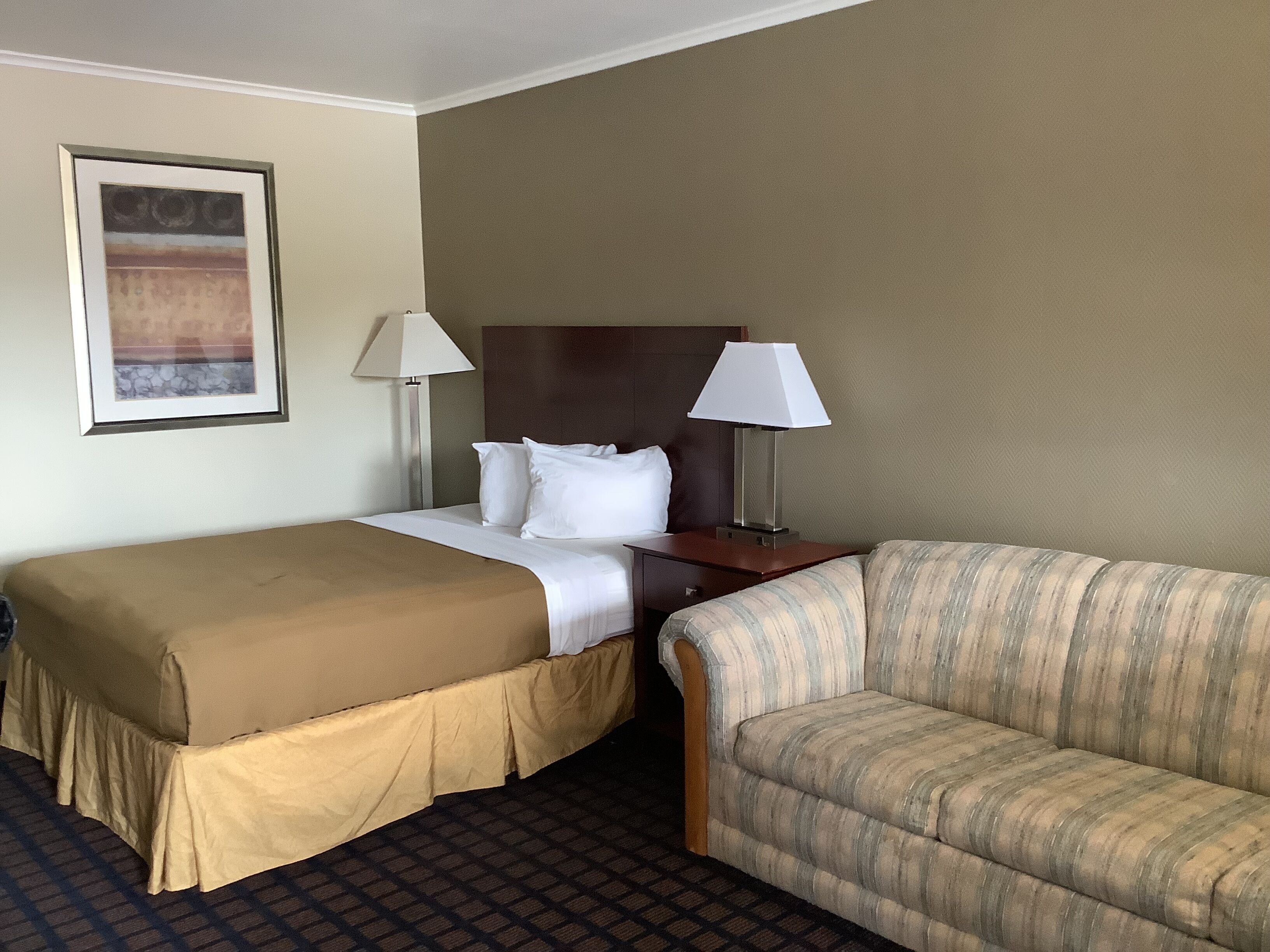 A hotel room with a double bed, two bedside lamps, a sofa, and a framed picture on the wall.