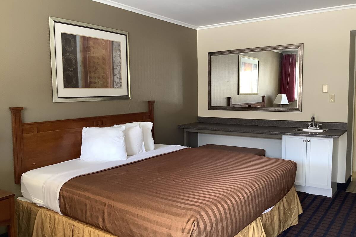 A hotel room with a bed, a desk, a mirror, and a framed picture on the wall.