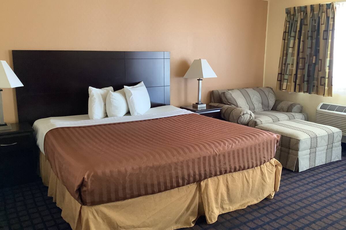 A hotel room with a large bed, a sofa, a nightstand, and a lamp.