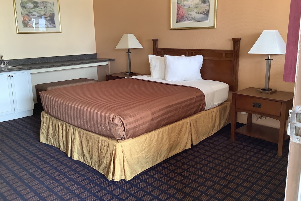 A hotel room with a bed, bedside tables, a desk, and a sink.