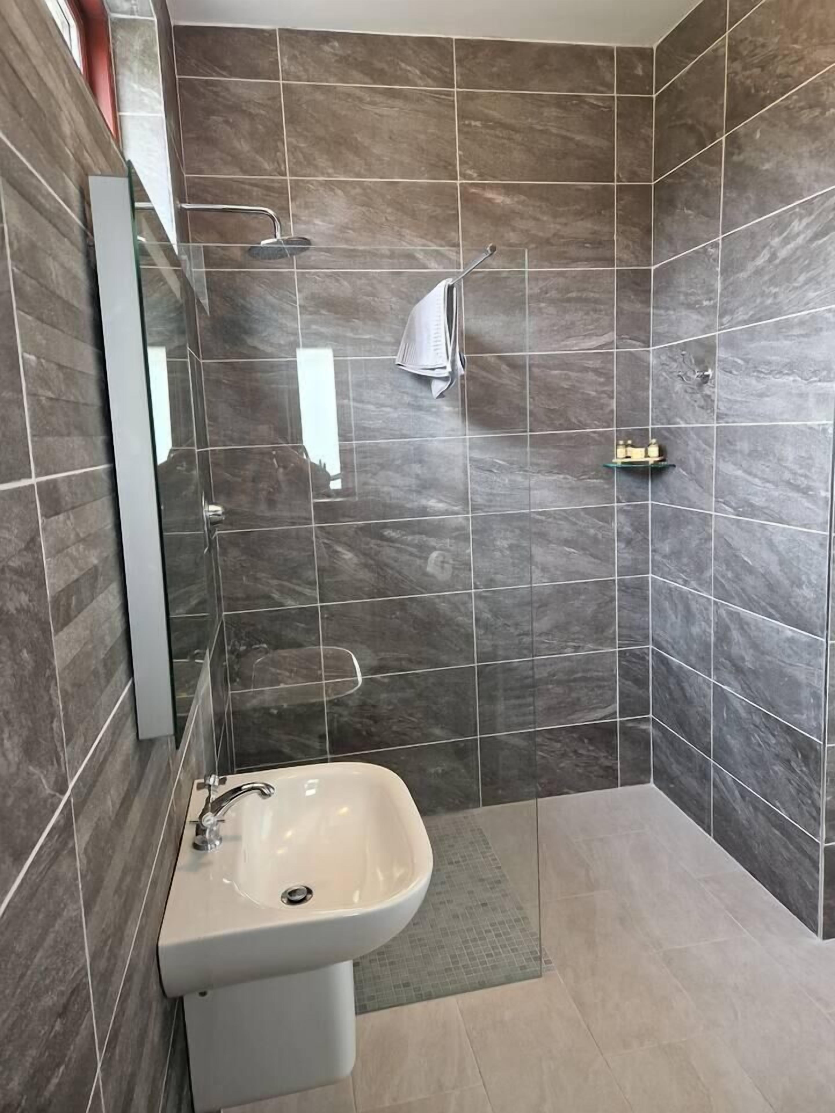 Een moderne badkamer met een wastafel in de hoek, een douchecabine met glazen wanden en een betegelde vloer.