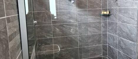 Een moderne badkamer met een wastafel in de hoek, een douchecabine met glazen wanden en een betegelde vloer.