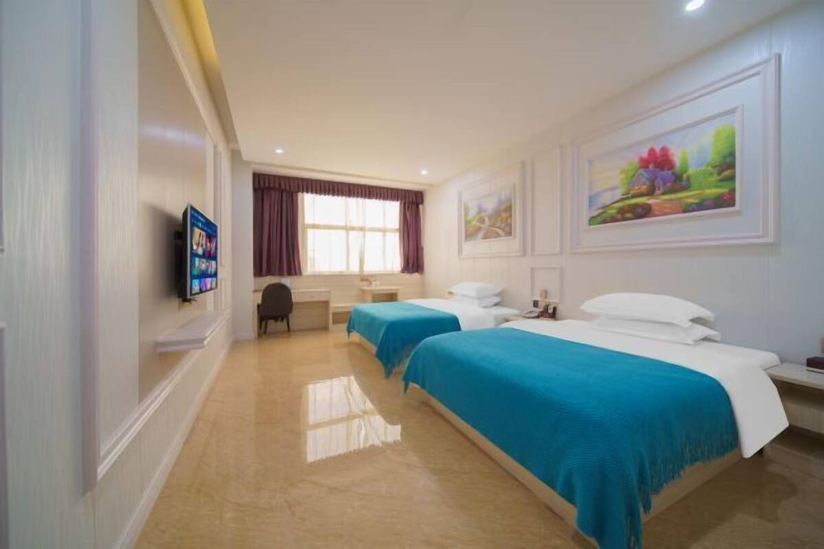 A hotel room with two beds, a desk, a chair, a TV, and artwork on the walls.