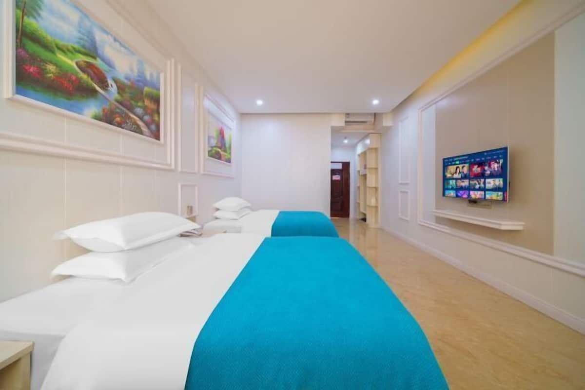 A hotel room with two beds, a TV on the wall, and artwork on the walls.