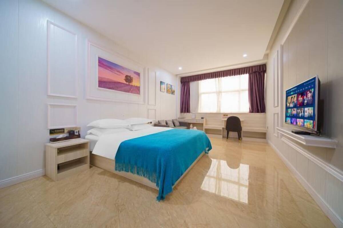 A hotel room with a bed, a desk, a chair, a TV, and artwork on the walls.