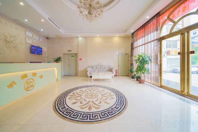 A hotel lobby with a reception desk, a sofa, a chandelier, and a large window.